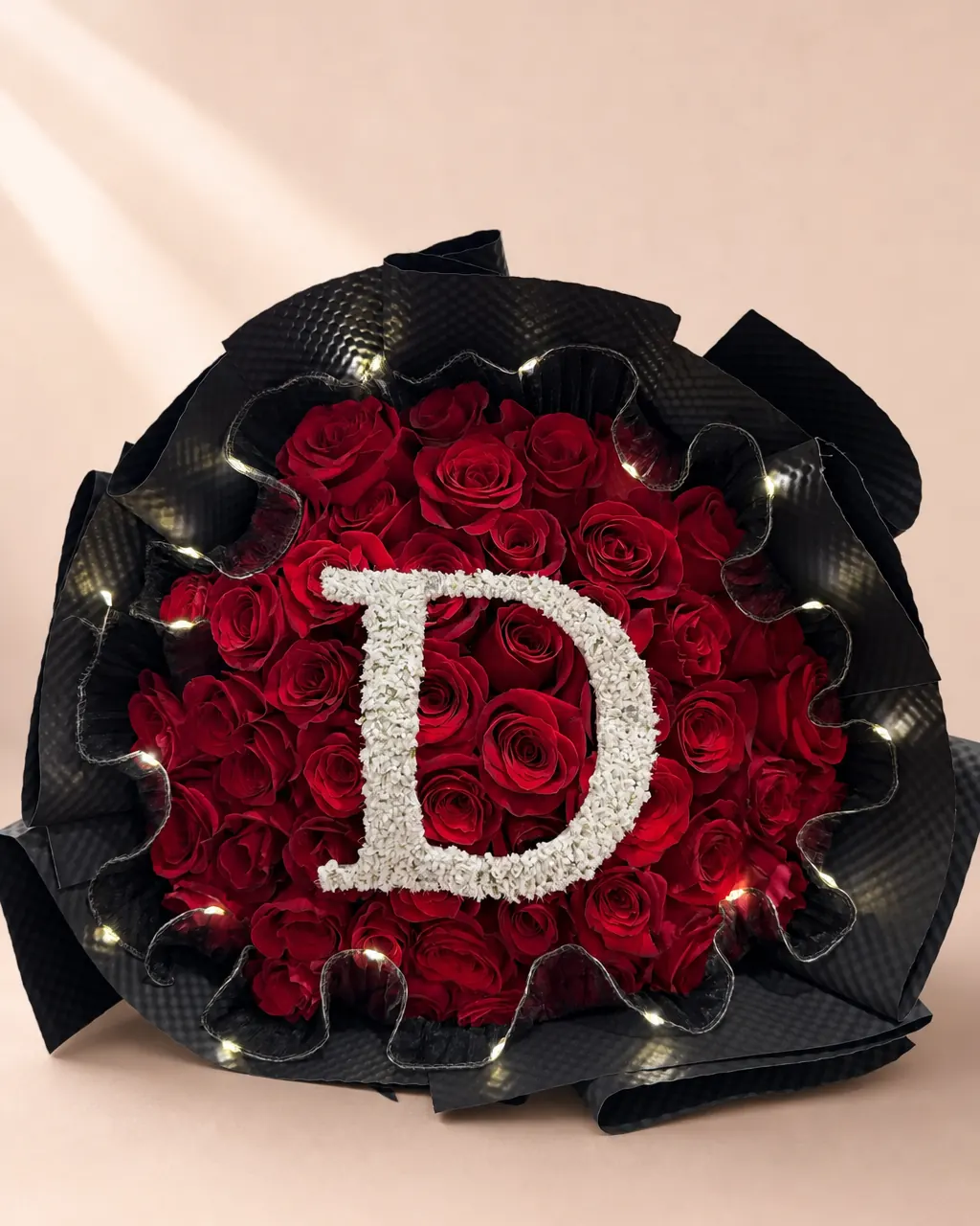 Marquee: fifty red roses in black wrap with a white initial made of tiny blooms and a ring of small LED lights