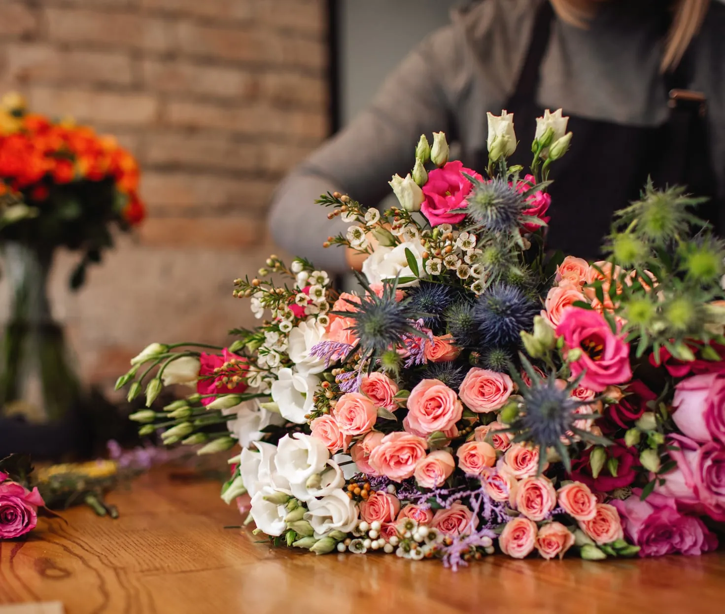 A florist hand-tying a bouquet of spray roses, lisianthus and blue thistle on a wooden workbench