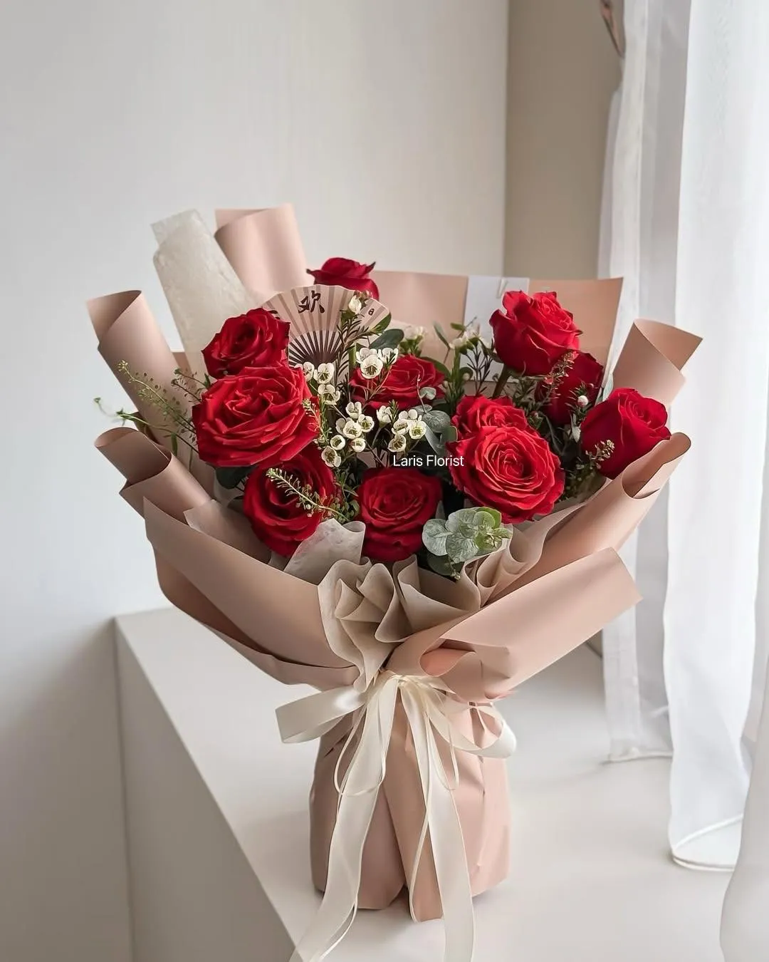 Red rose bouquet with white waxflower wrapped in blush paper and tied with ribbon