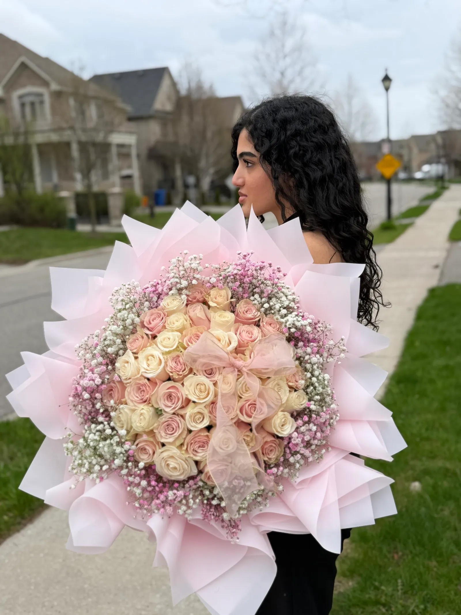 Woman holding a large pink and cream rose bouquet with baby's breath on a residential street