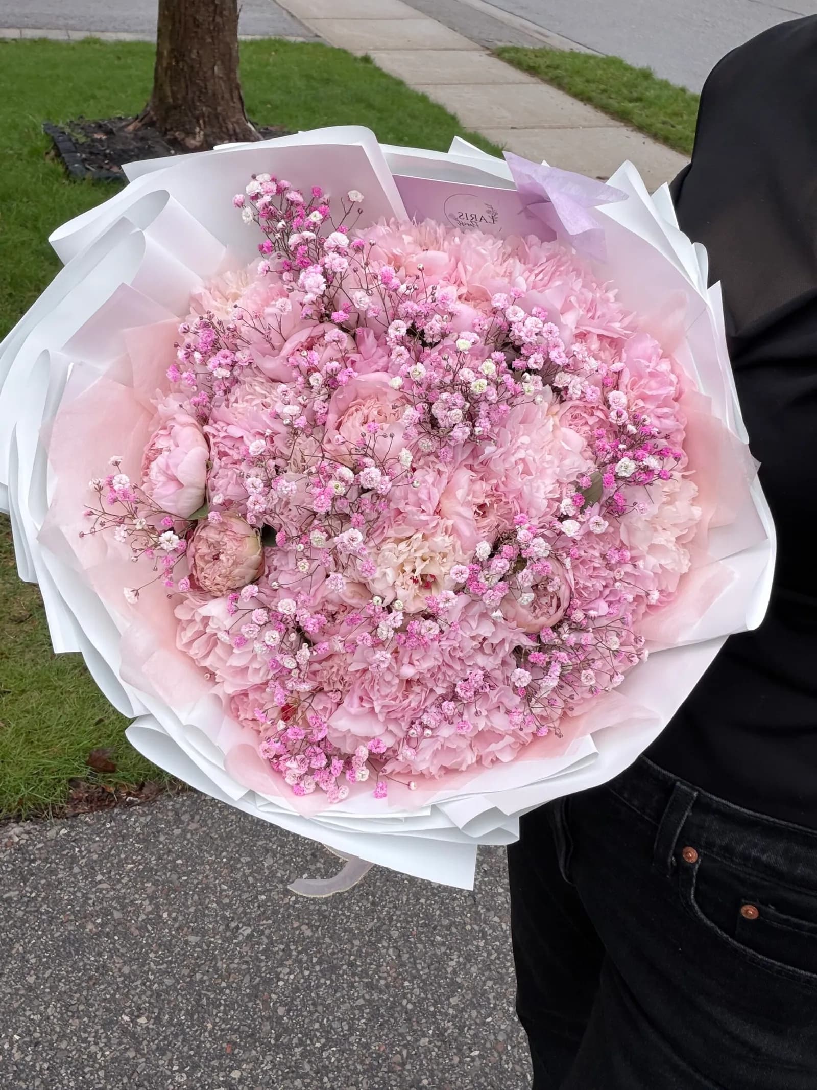 Pink baby's breath bouquet in white wrapping held outdoors