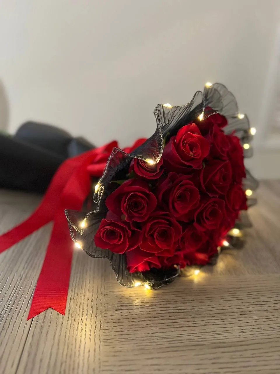 Red rose bouquet with black ruffled wrap, red ribbon and fairy lights