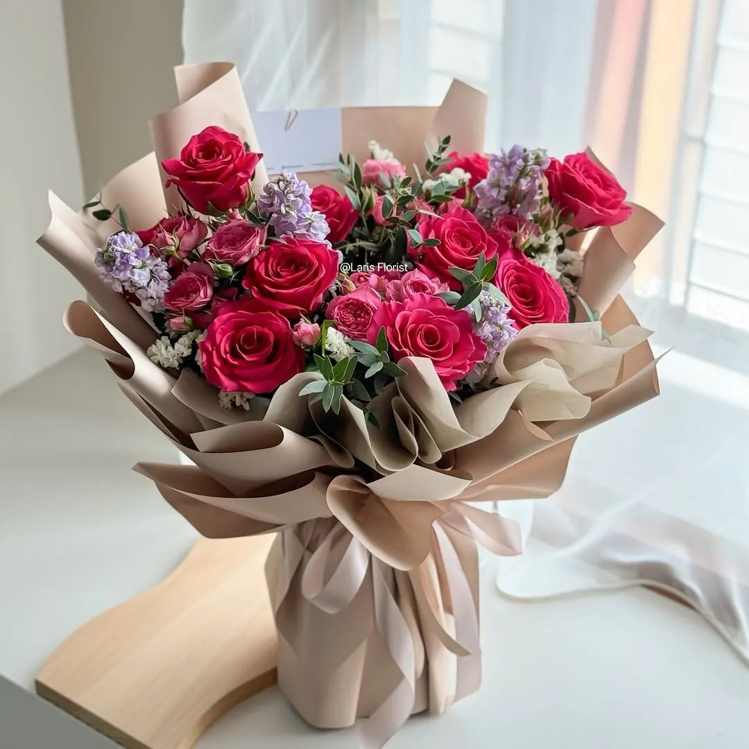 Bouquet of red and pink roses with lilac stock wrapped in blush paper