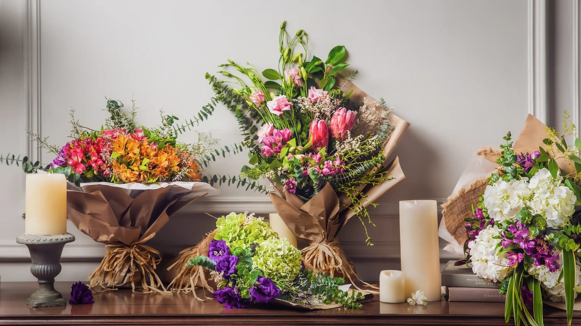 Several wrapped bouquets and pillar candles arranged on a wooden mantel