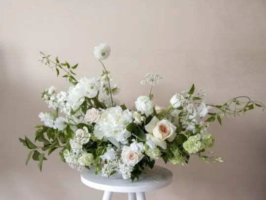 Low garden-style white centrepiece of roses, lisianthus and greenery on a pedestal