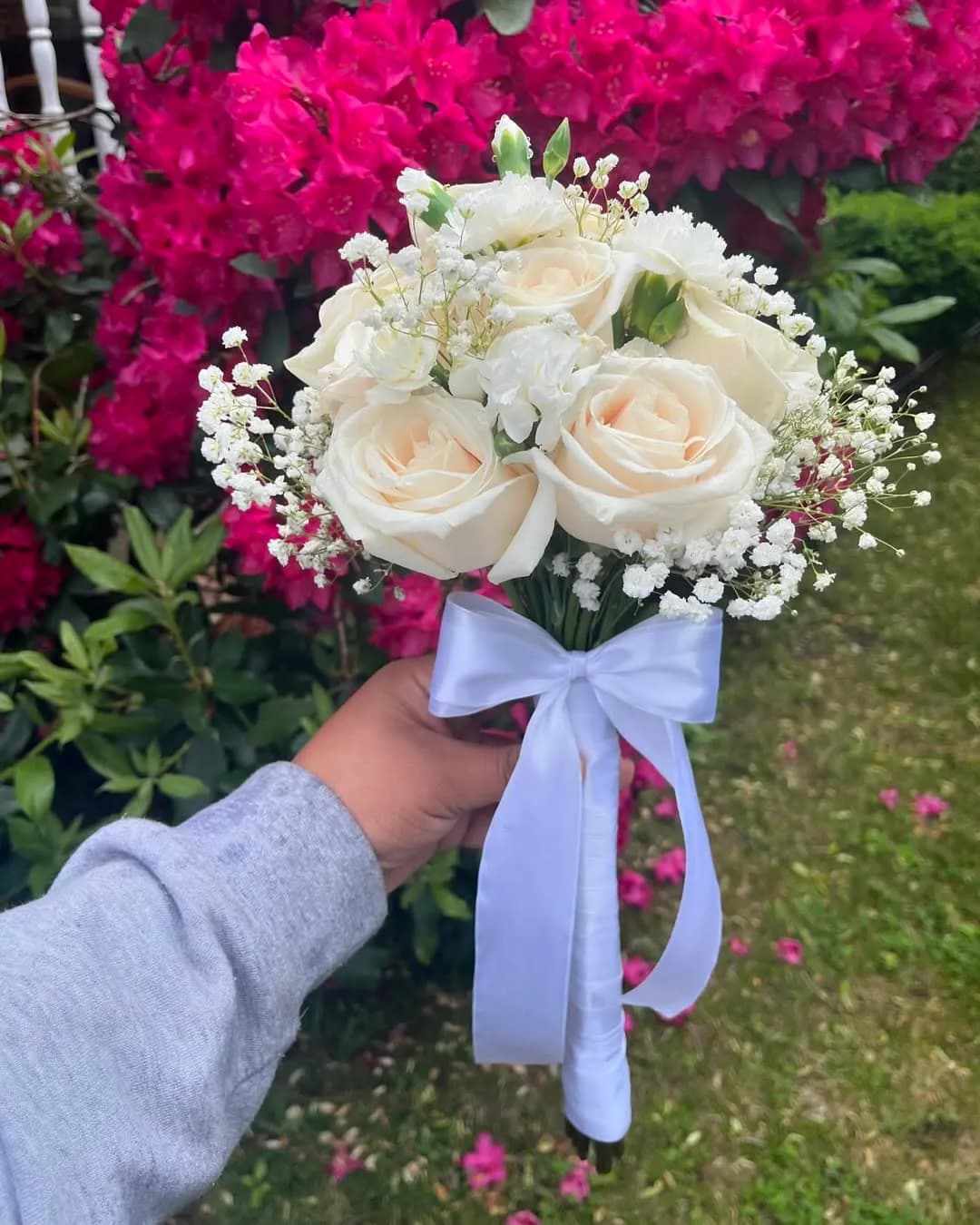 Hand holding a white rose and baby's breath posy tied with a white ribbon
