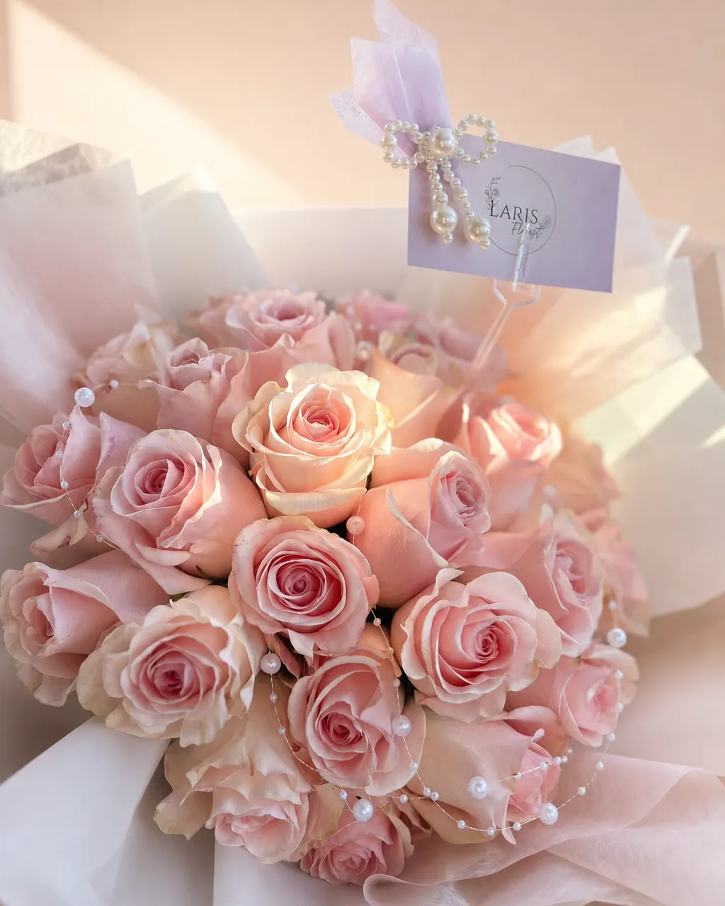 Blush and Pearls: twenty-five pink roses with pearl strands and a Laris card in white and blush wrap, on a blush backdrop