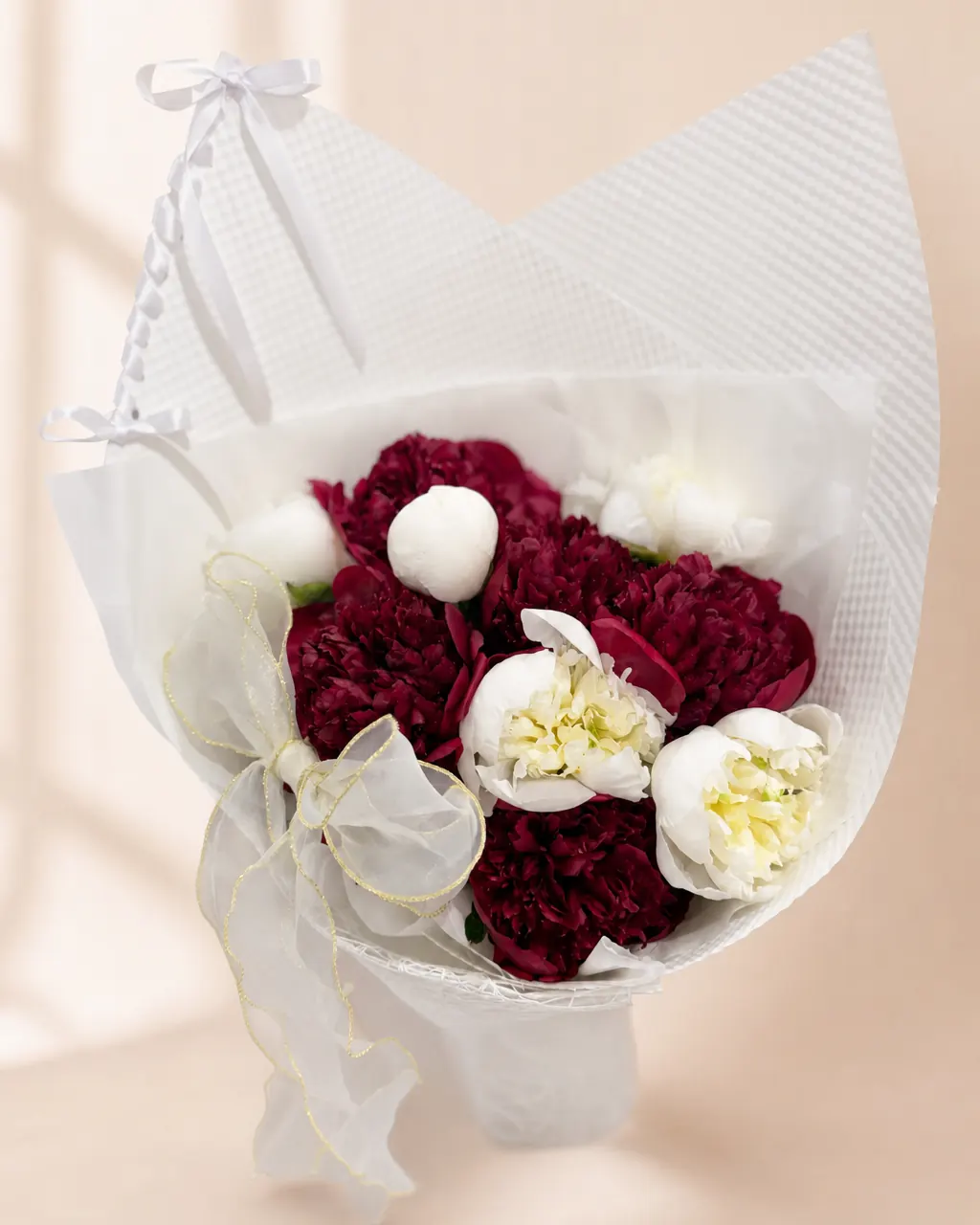 Claret and Cream: Red and white peonies in a white wrap, photographed on a blush backdrop
