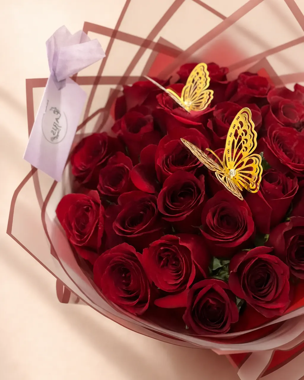 Gilded Wings: 25 premium red roses with gold butterflies, photographed on a blush backdrop